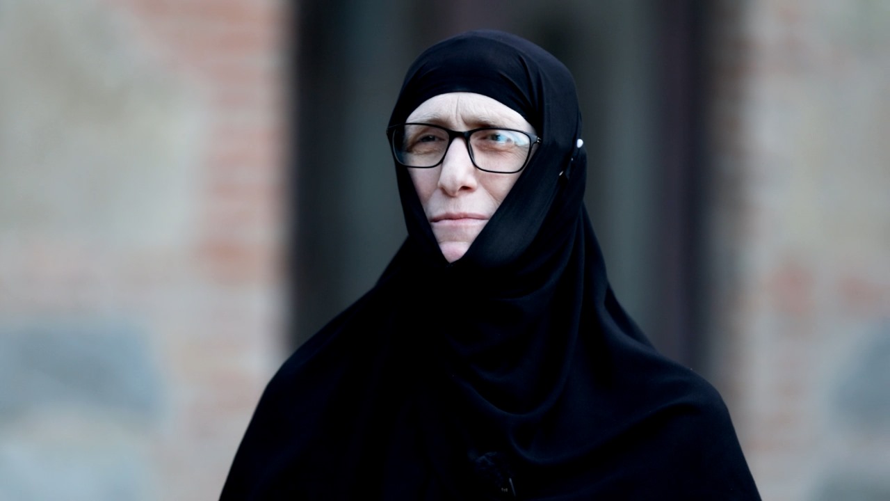 <p style="text-align: justify">დღევანდელი რუბრიკის "ადამიანები ისტორიით“ სტუმარია <strong><em>იღუმენია მარიამი</em></strong> (ჯაფარიძე) - ადამიანი, რომლის ცხოვრება თავისთავად არის გზა, ტკივილითა და სიყვარულით სავსე, შინაგანი ბრძოლიდან სულიერ სიმშვიდემდე.</p><p style="text-align: justify">მისი საერო სახელი ლელა იყო. აქტიური, განათლებული და მოაზროვნე ახალგაზრდა ქალი, რომელმაც საბჭოთა კავშირის ბოლო წლებში მიიღო განათლება ივანე ჯავახიშვილის სახელობის თბილისის სახელმწიფო უნივერსიტეტში, ფილოლოგიის ფაკულტეტზე. ამის შემდეგი პერიოდი ის იყო მორჩილი ელენე და პარალელურად მუშაობდა საპატრიარქოს გამომცემლობაში.</p><p style="text-align: justify">1994 წელს ელენემ მიიღო სამონაზვნო სახელი - ემილია, ხოლო 2000 წელს, ეკლესიური მსახურების მრავალი წლის შემდეგ, ეკურთხა როგორც მონაზონი მარიამი. უკვე 2016 წელს მას მიენიჭა იღუმენიას ხარისხი.</p><p style="text-align: justify">სულიერების გზა და პირადი თავგადასავალი</p><p style="text-align: justify">ვიდეოში იღუმენია მარიამი გულწრფელად და ღრმად საუბრობს იმ გზაზე, რომელიც გაიარა - როგორ დაუბრუნდა ეკლესიას, როგორ იგრძნო შინაგანი მოწოდება, რომ გაჩერებულიყო და ცხოვრება ღმერთისთვის მიეძღვნა.</p><p style="text-align: justify">"საღვთისმსახურო ცხოვრება - ეს არის მუდმივი ყოფნა ჭეშმარიტებასთან", - ამბობს დედაო.</p><p style="text-align: justify"><strong>ეროვნული მოძრაობის დღეები და გადამწყვეტი მომენტი</strong></p><p style="text-align: justify">დედა მარიამი ასევე იხსენებს 1980–90-იანი წლების ეროვნულ მოძრაობაში მონაწილეობას. ის ჰყვება იმ შიგნით გამანადგურებელ, მაგრამ საბოლოოდ განმანათლებელ მომენტზე, როცა გადაწყვიტა, რომ ბრძოლა ქუჩაში აღარ იყო მისი გზა და რომ სულიერი ბრძოლა იყო ის, რასაც უნდა შესწიროს თავი.</p><p style="text-align: justify"><strong>გზის განმსაზღვრელი ადამიანები და იდეები</strong></p><p style="text-align: justify">აღსანიშნავია მისი საუბარი უწმინდესის ილია II-ის როლზე მის ცხოვრებაში. იგი უდიდეს მადლიერებას გამოხატავს და ამბობს, რომ მისგან უსაზღვრო სითბო და სიბრძნე მიიღო.</p><p style="text-align: justify">დედა მარიამი საუბრობს მერაბ მამარდაშვილის, ჰერმან ჰესეს და სხვა მოაზროვნეების გავლენაზეც - ადამიანებზე და ტექსტებზე, რომლებმაც მის სულიერ ჩამოყალიბებას ხელი შეუწყვეს.</p><p style="text-align: justify"><strong>რას ნიშნავს ევროპა დედა მარიამისთვის</strong></p><p style="text-align: justify">ევროპული ხელოვნება, მწერლობა, ფილოსოფია მისთვის არის სამყარო, რომელშიც ის გაიზარდა ჩამოყალიბდა პიროვნულად და მოემზადა მისი მთავარი გადაწყვეტილებისთვის.</p><p style="text-align: justify"><strong>დღევანდელობა და საზოგადოება: მორალური დილემები და პოლარიზაცია</strong></p><p style="text-align: justify">"პოლარიზაციამ შეიძლება ადამიანი ფსიქიკურ სიღატაკემდე მიიყვანოს", - ამბობს იღუმენია მარიამი.</p><p style="text-align: justify">მისი შეფასებით, თანამედროვე საზოგადოება ხშირად ივიწყებს იმას, რომ ცხოვრების ყოველი წამი ძვირფასია და ის არ უნდა დაიხარჯოს შუღლსა და დაპირისპირებაში.</p><p style="text-align: justify">"ადამიანის სიცოცხლე არ უნდა დაიხარჯოს, არც ერთი წამი არ უნდა დაიხარჯოს ადამიანის ცხოვრების რაღაცასთან დაპირისპირებაში" - ამბობს დედა მარიამი.</p><div class="iframe-wrapper"><iframe src="https://www.youtube.com/embed/wOeHqQqbzhs?si=SzaBhGoEWjARbAvi" frameborder="0" allowfullscreen="true" width="560" height="315" title="YouTube video player" allow="accelerometer; autoplay; clipboard-write; encrypted-media; gyroscope; picture-in-picture; web-share"></iframe></div>